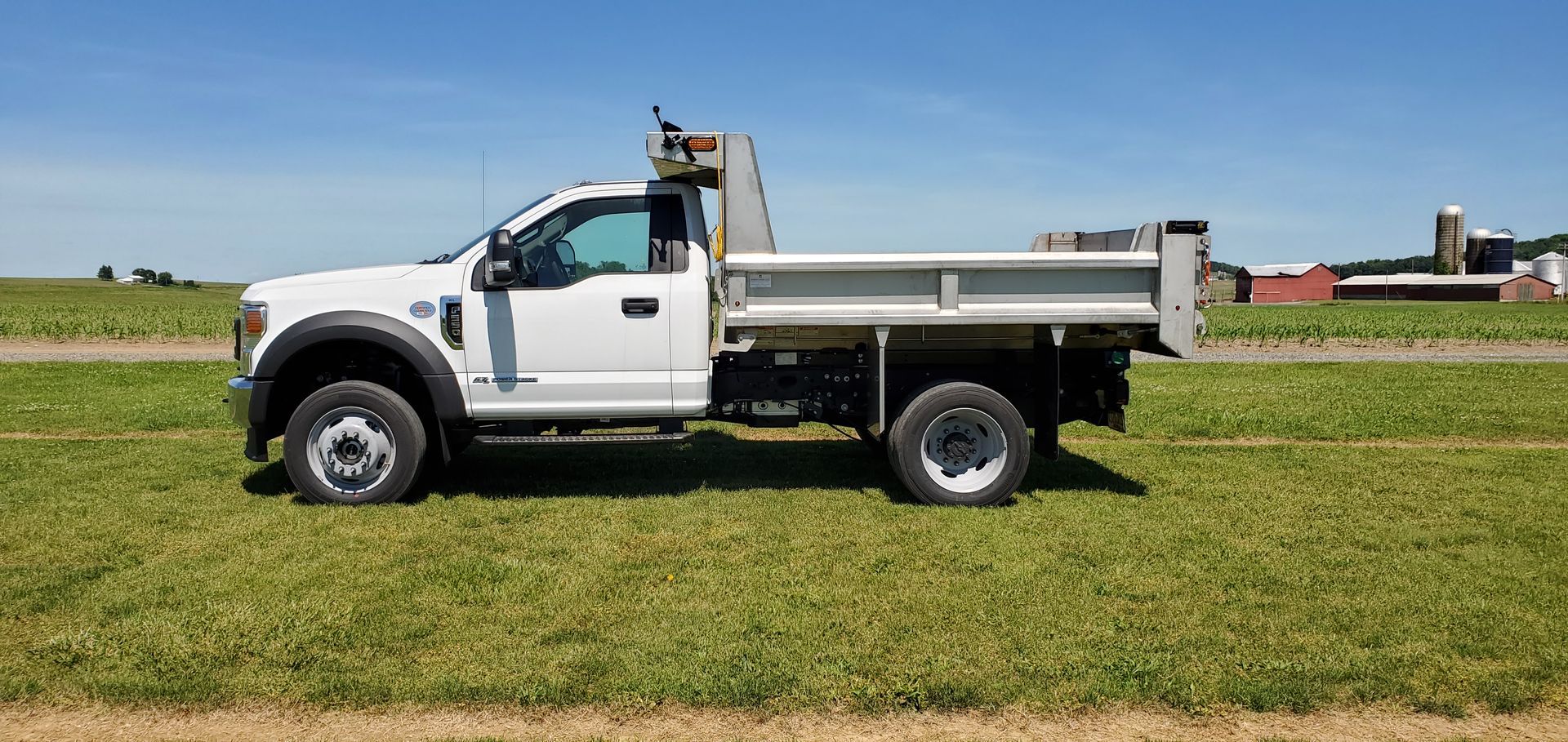 A white dump truck is parked in a grassy field.
