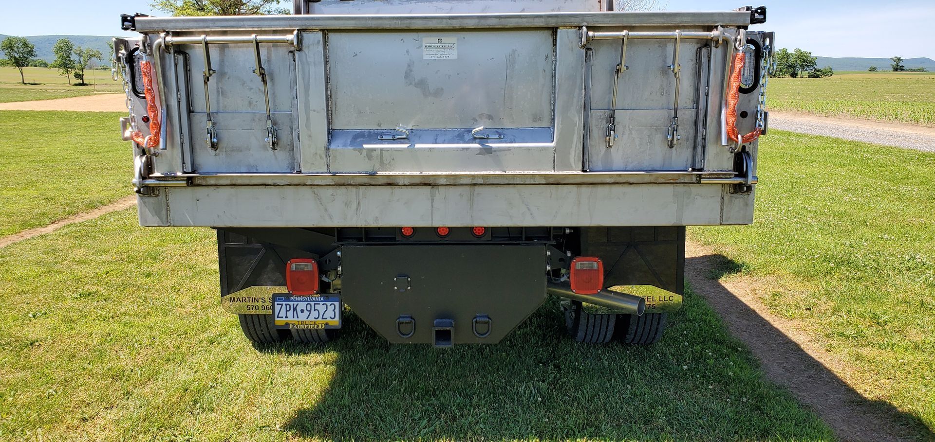 The back of a dump truck is parked in a grassy field.