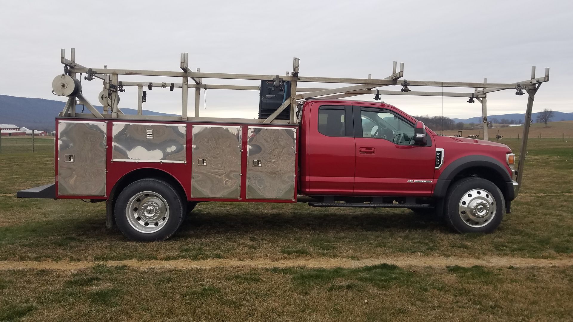 A red truck with a ladder rack on top of it is parked in a field.