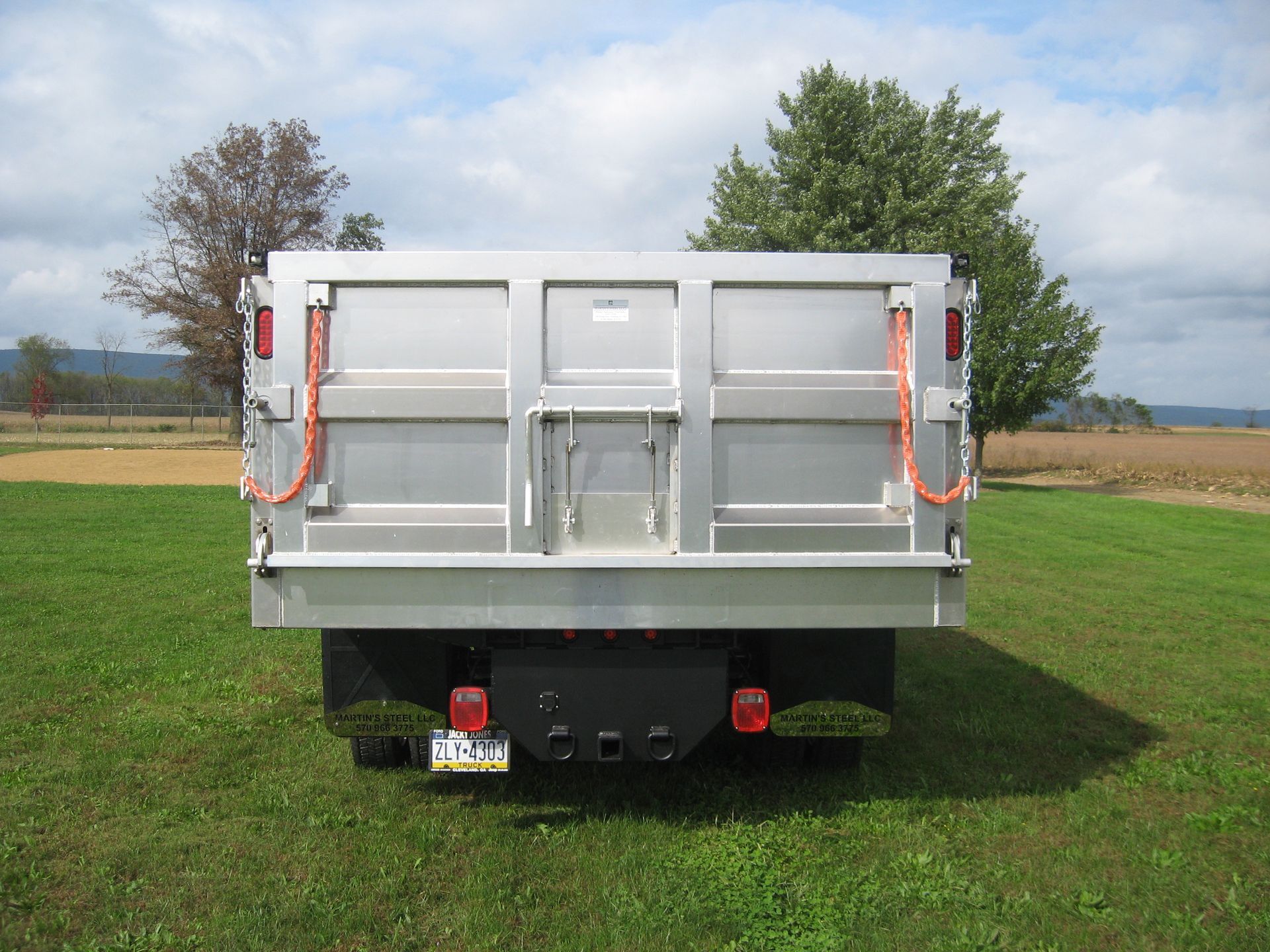 A silver dump truck is parked in a grassy field