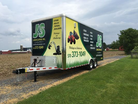 A j & s trailer is parked in a grassy field