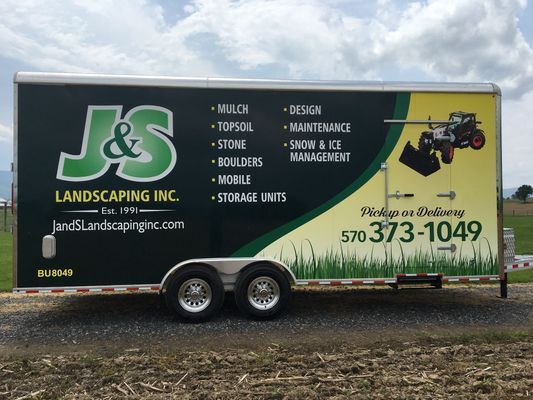 A trailer for j & s landscaping inc. is parked in a field