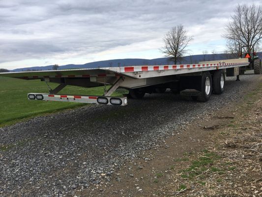A flatbed trailer is parked on the side of a gravel road.