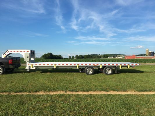 A truck is towing a flatbed trailer in a grassy field.