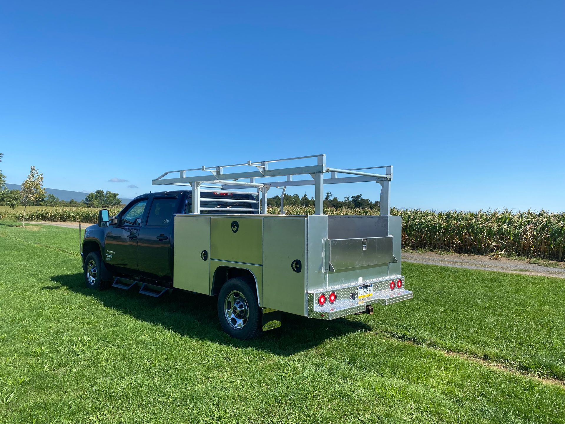 A truck with a ladder rack on the back is parked in a grassy field.