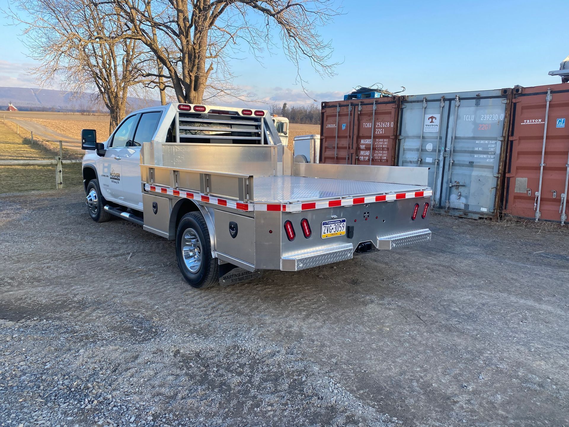 A silver truck with a flat bed is parked in a gravel lot.