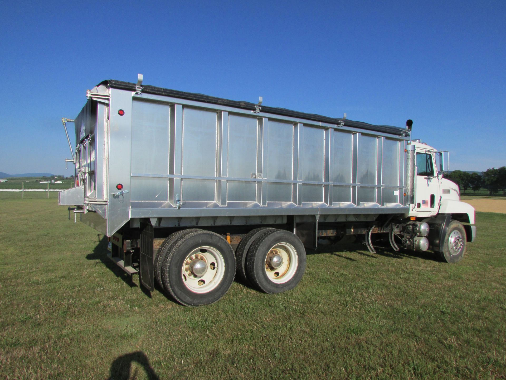 A white dump truck is parked in a grassy field.