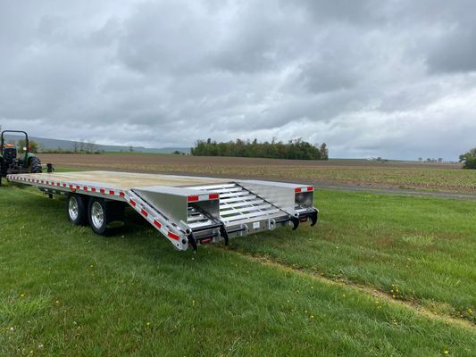 A flatbed trailer is parked in a grassy field next to a tractor.