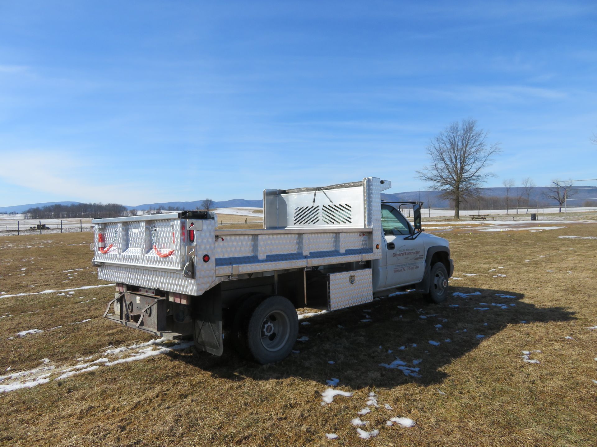 A white dump truck is parked in a grassy field.