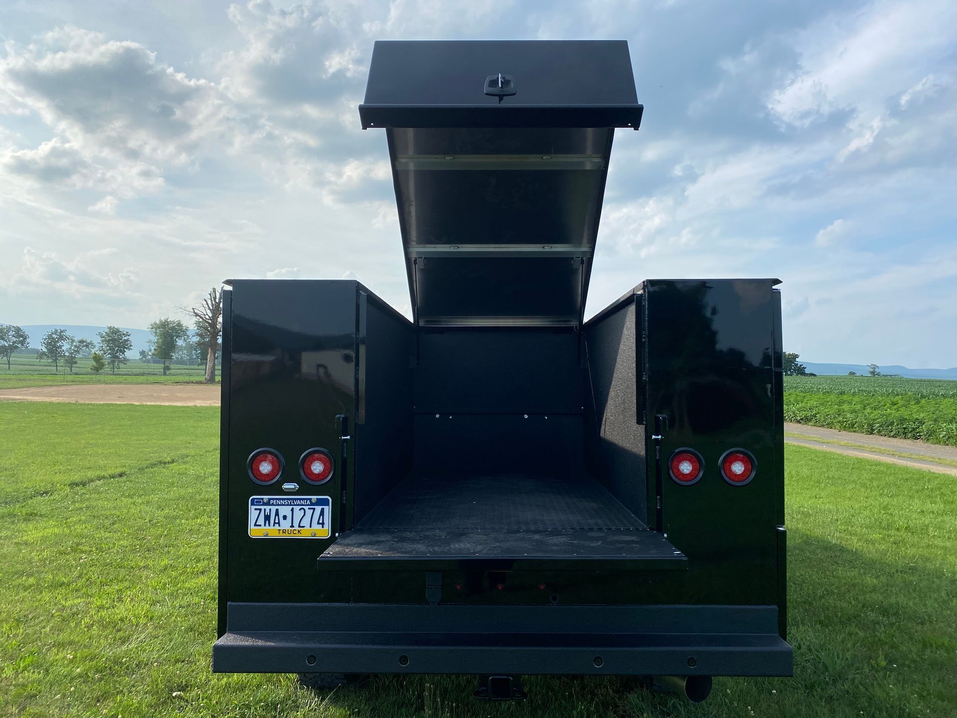 A black truck with the back door open is parked in a grassy field.