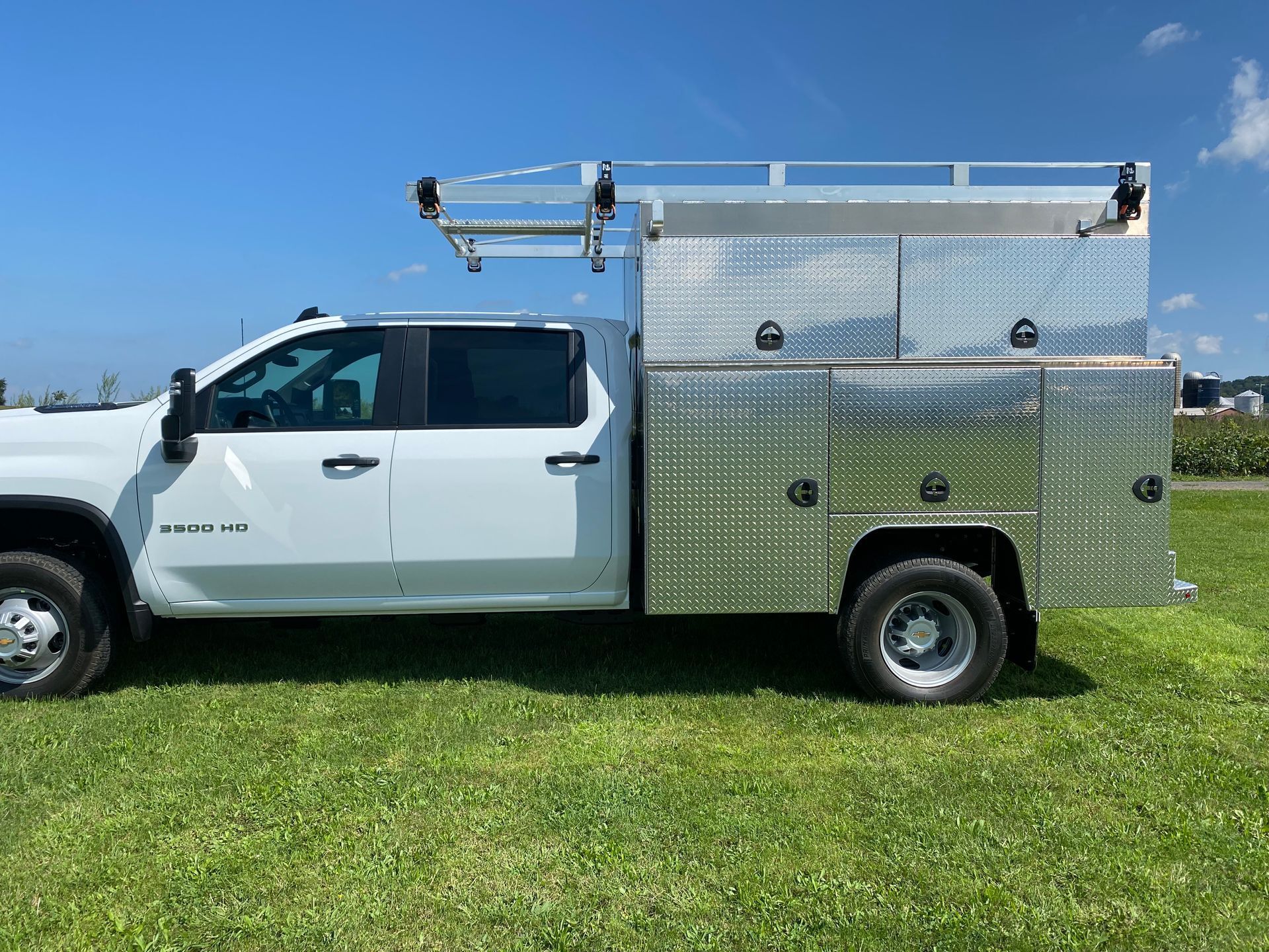 A white truck with a ladder on top of it is parked in a grassy field.