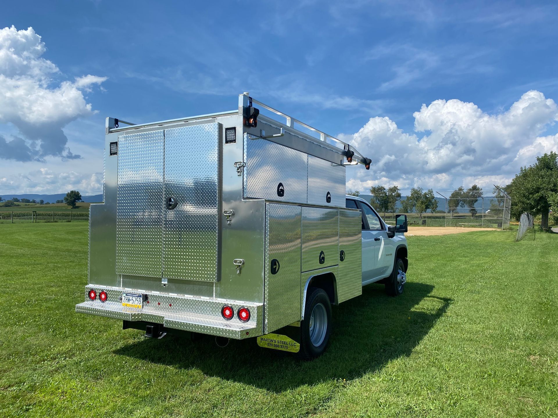 A silver utility truck is parked in a grassy field.