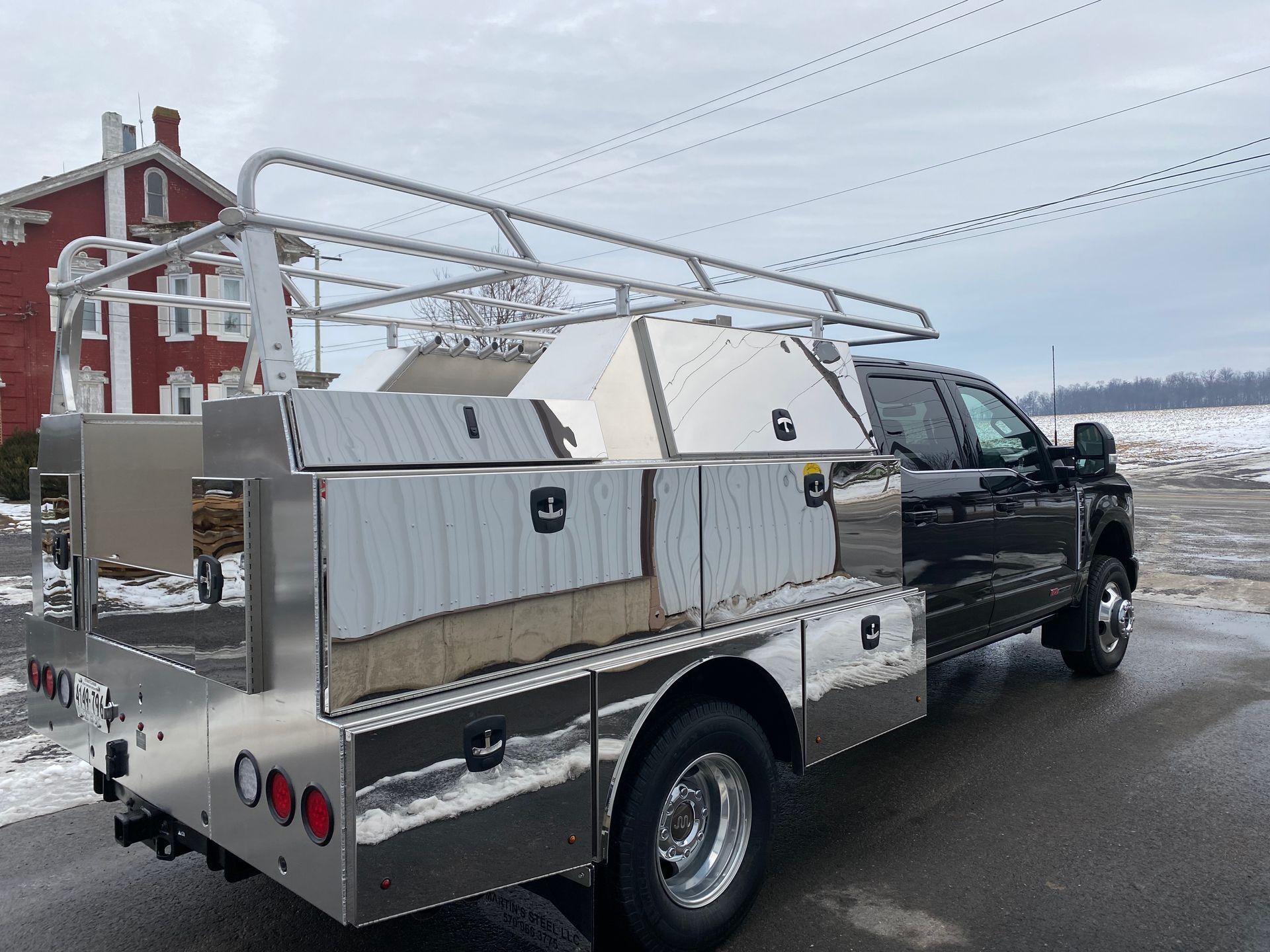 A black truck with a stainless steel bed is parked on the side of the road.