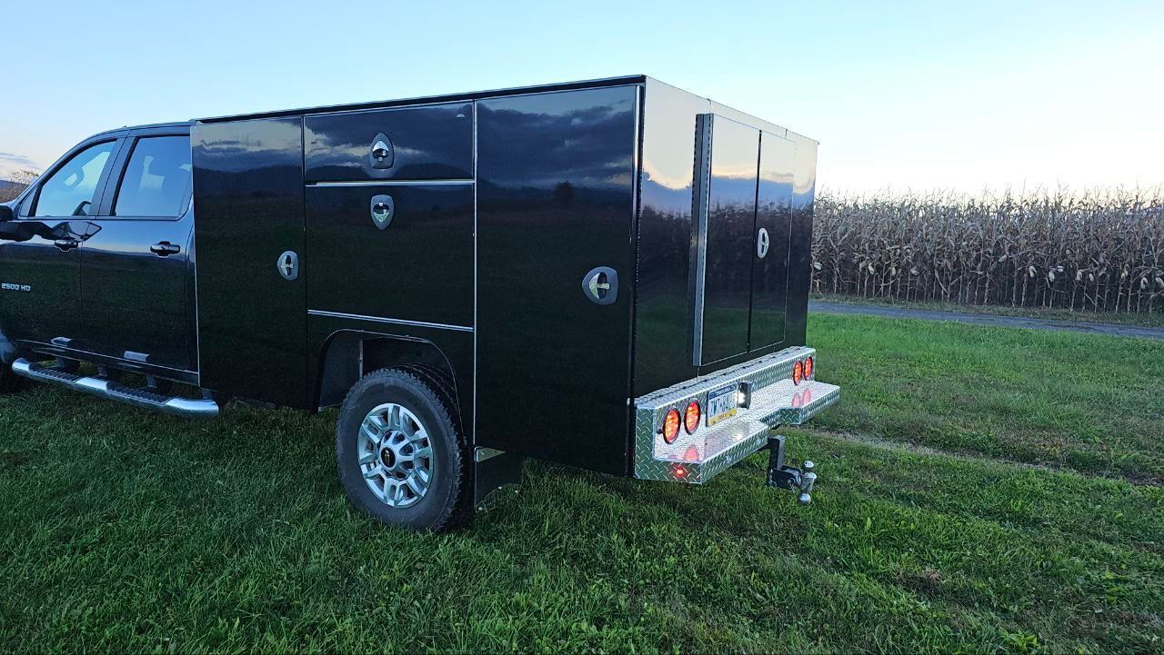 A black truck with a trailer attached to it is parked in a grassy field.