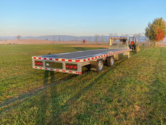 A flatbed trailer is parked in a grassy field next to a tractor.