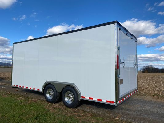 A white trailer is parked on the side of a road in a field.