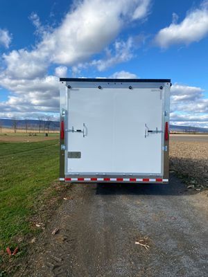 A white trailer is parked on the side of a dirt road.