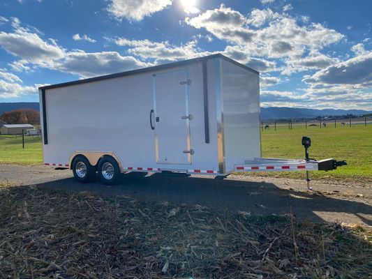 A white trailer is parked on the side of a road in a field.