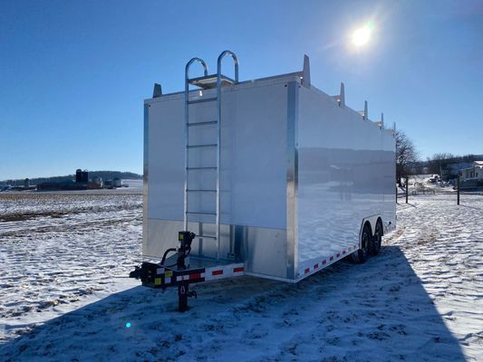 A white trailer with a ladder attached to it is parked in the snow.