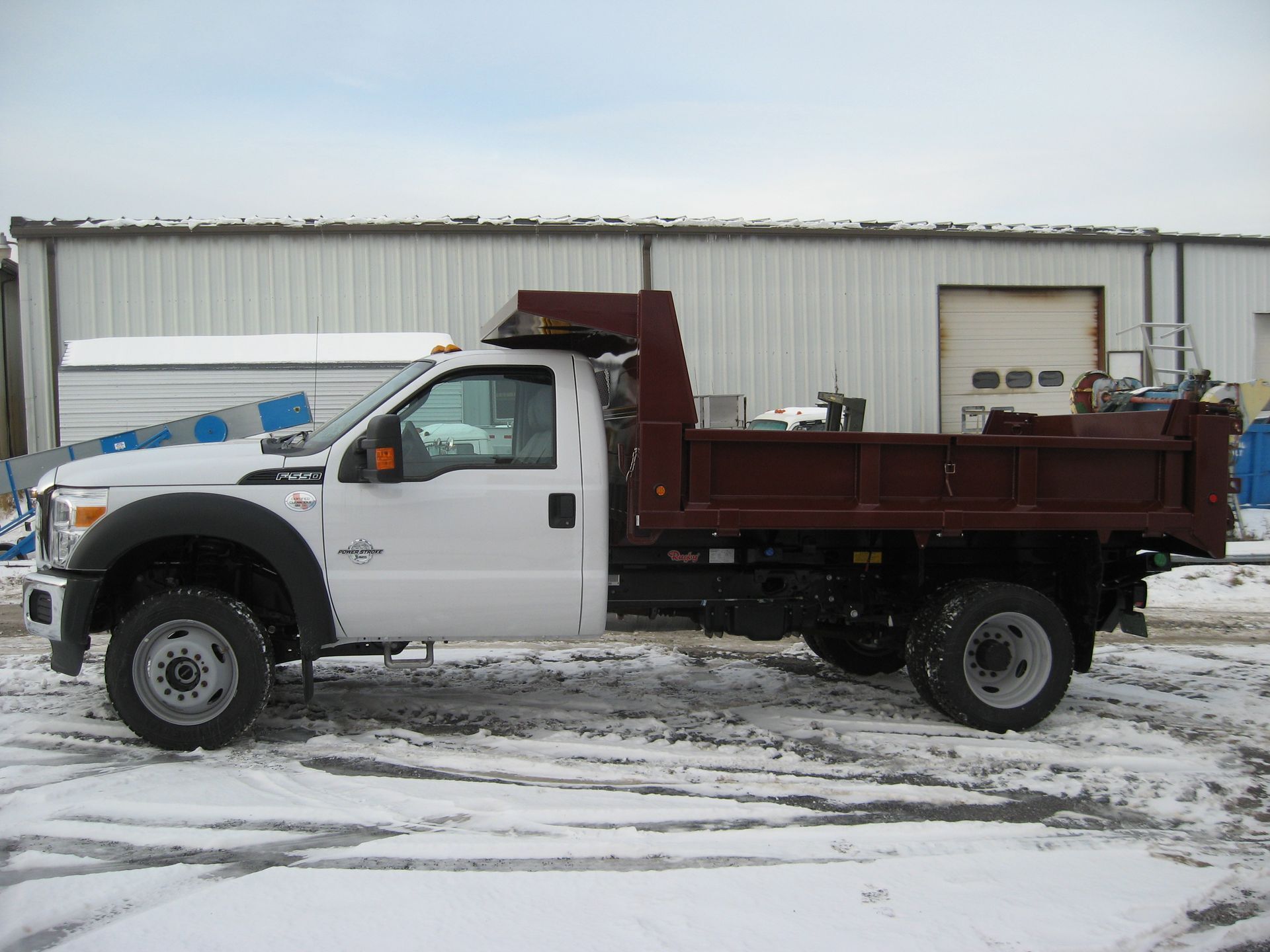 A white dump truck is parked in the snow in front of a building
