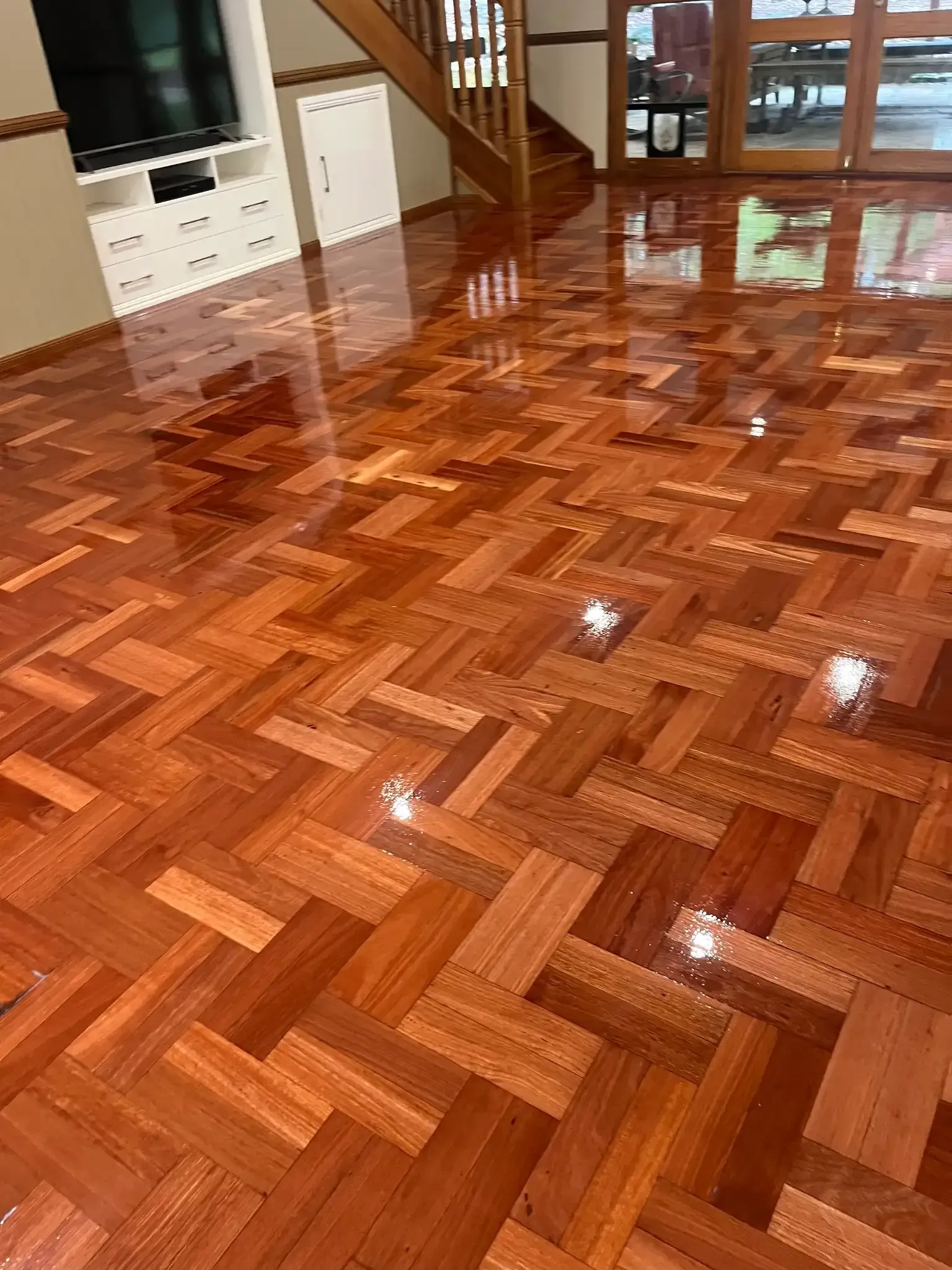 Shiny red parquet floor in a living room, reflecting light. White cabinets and a staircase are visible. — Toowoomba Polished Floors in Dalby, QLD