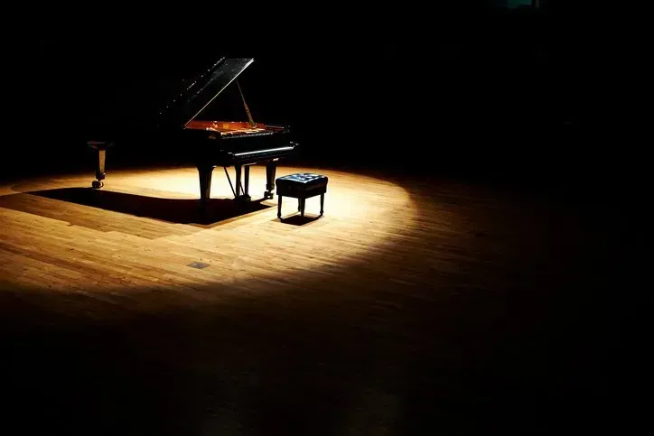 a grand piano is sitting on a wooden stage under a spotlight