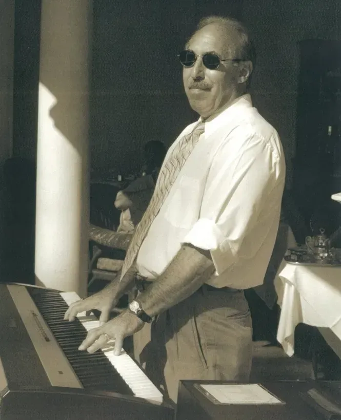 Bob Barry wearing sunglasses is playing a piano