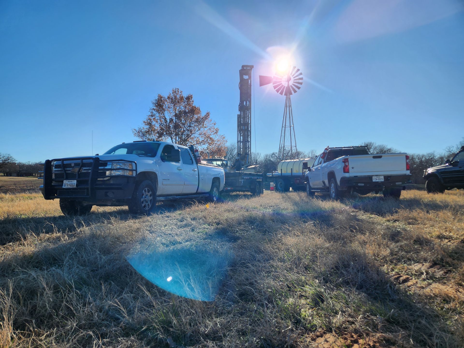 Two trucks are parked in a field next to a windmill.