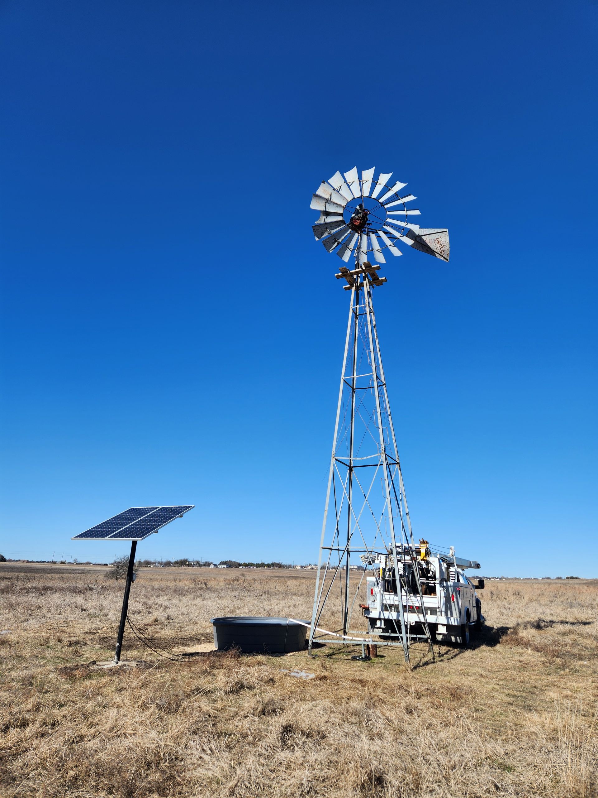 A windmill is sitting in the middle of a field next to a solar panel.