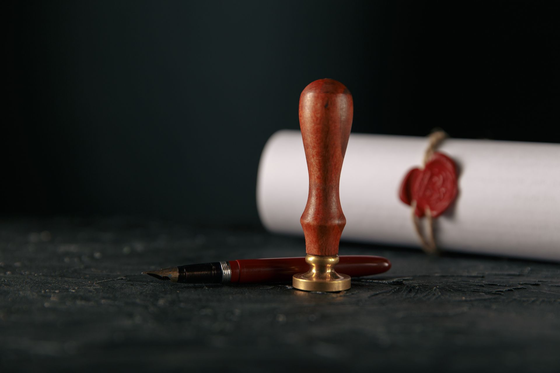 A stamp and a pen are on a table next to a scroll with a wax seal.