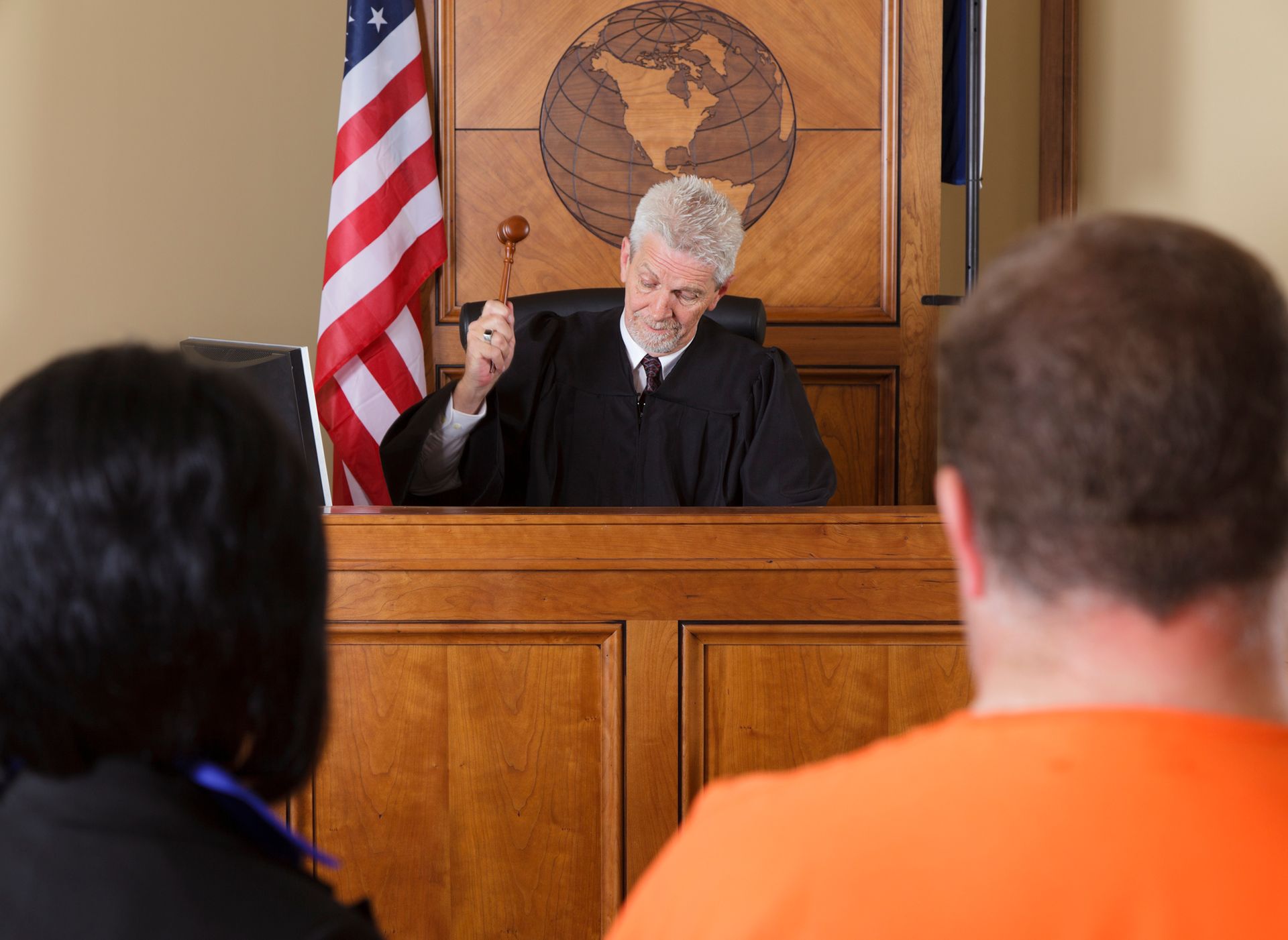 A man in an orange shirt is sitting in front of a judge holding a gavel