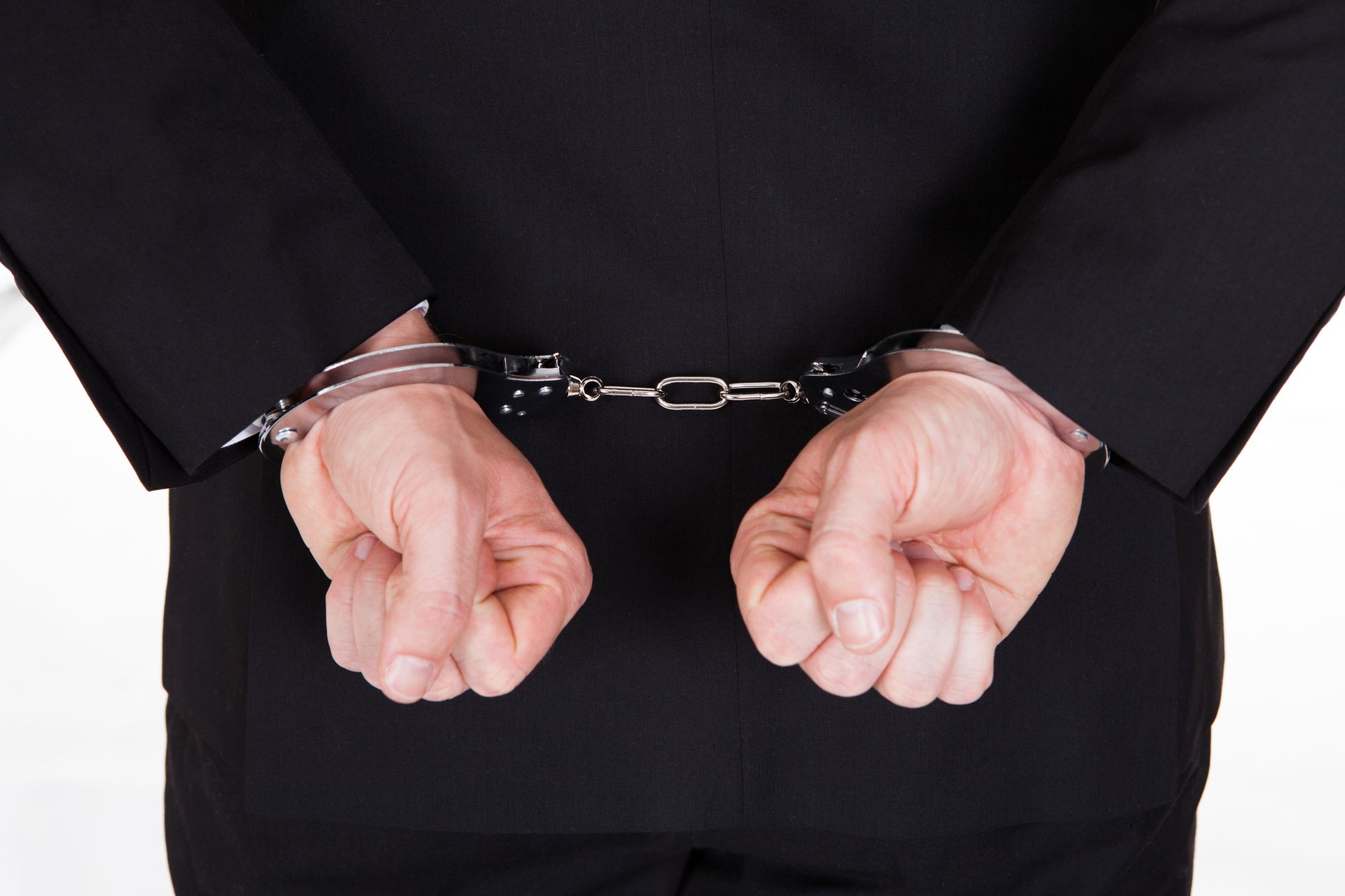 A man in a suit has his hands in handcuffs