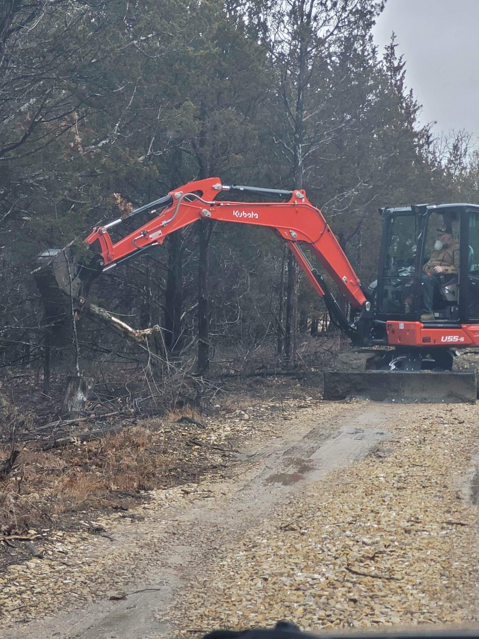 A red and black excavator is driving down a dirt road.