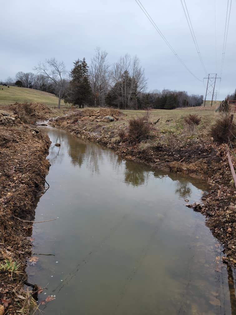 A small stream running through a field with power lines in the background.