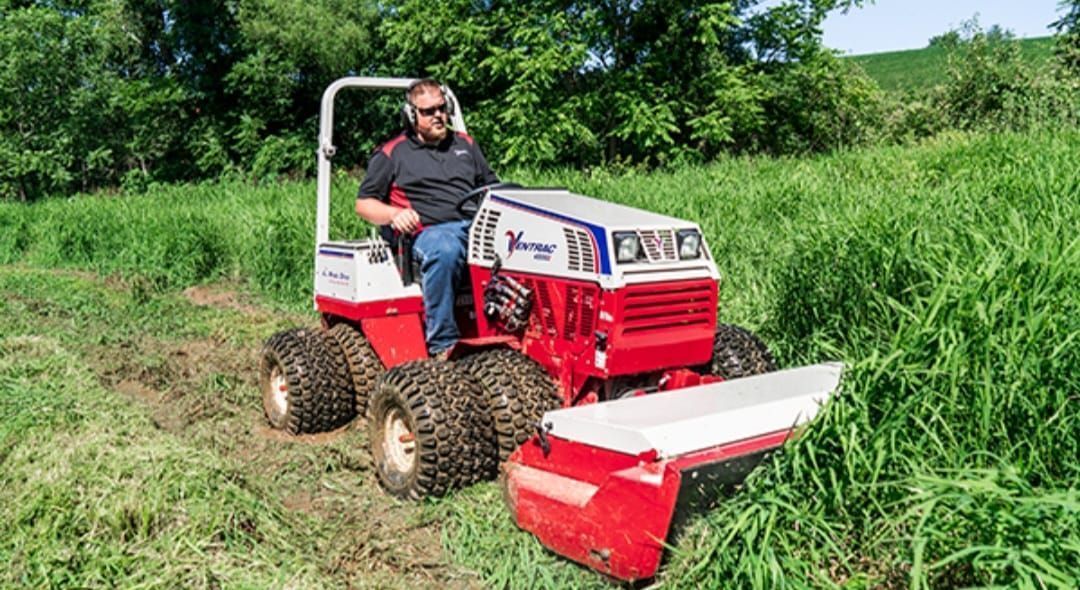 A man is riding a tractor through a grassy field.
