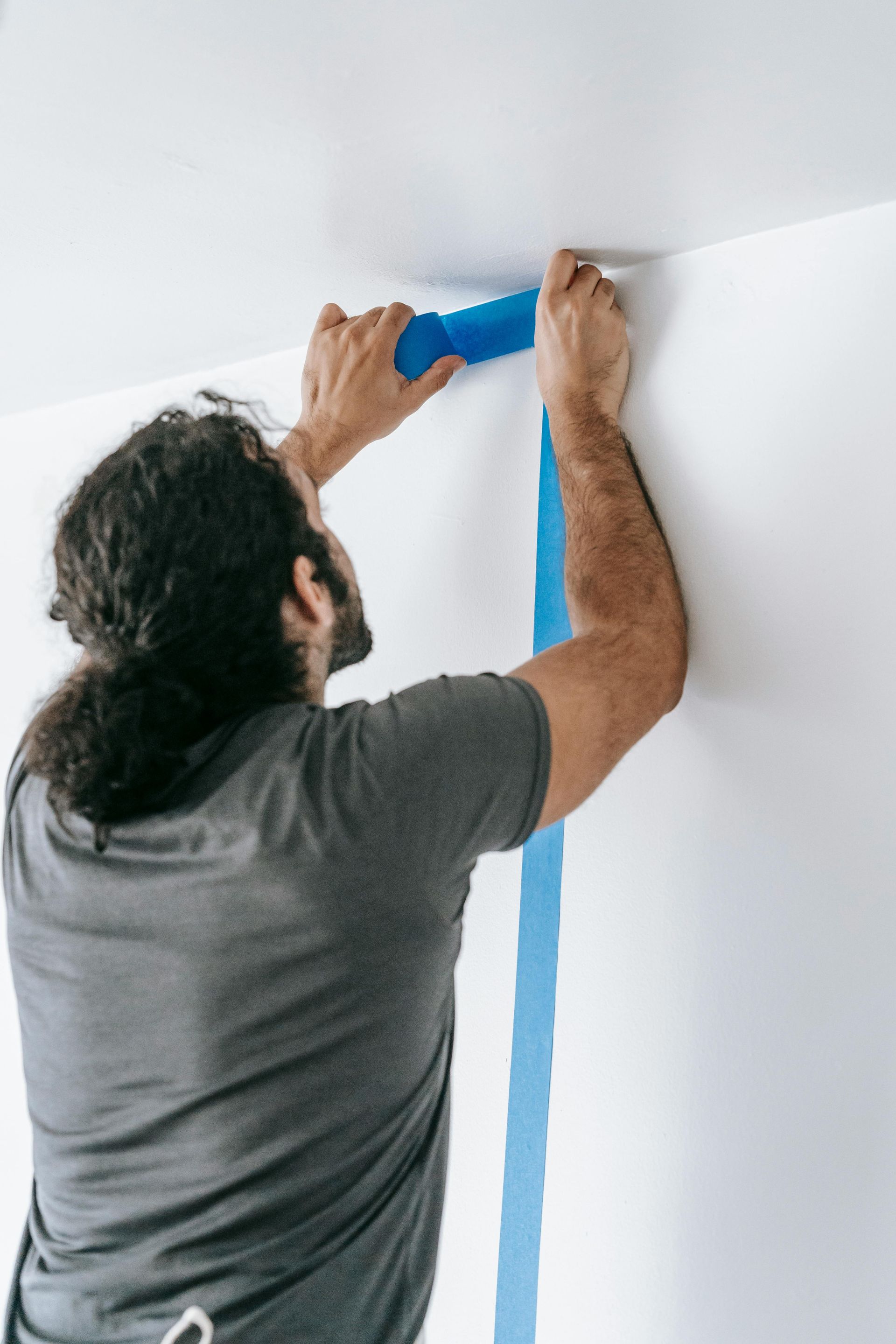 A man is painting a wall with blue tape.