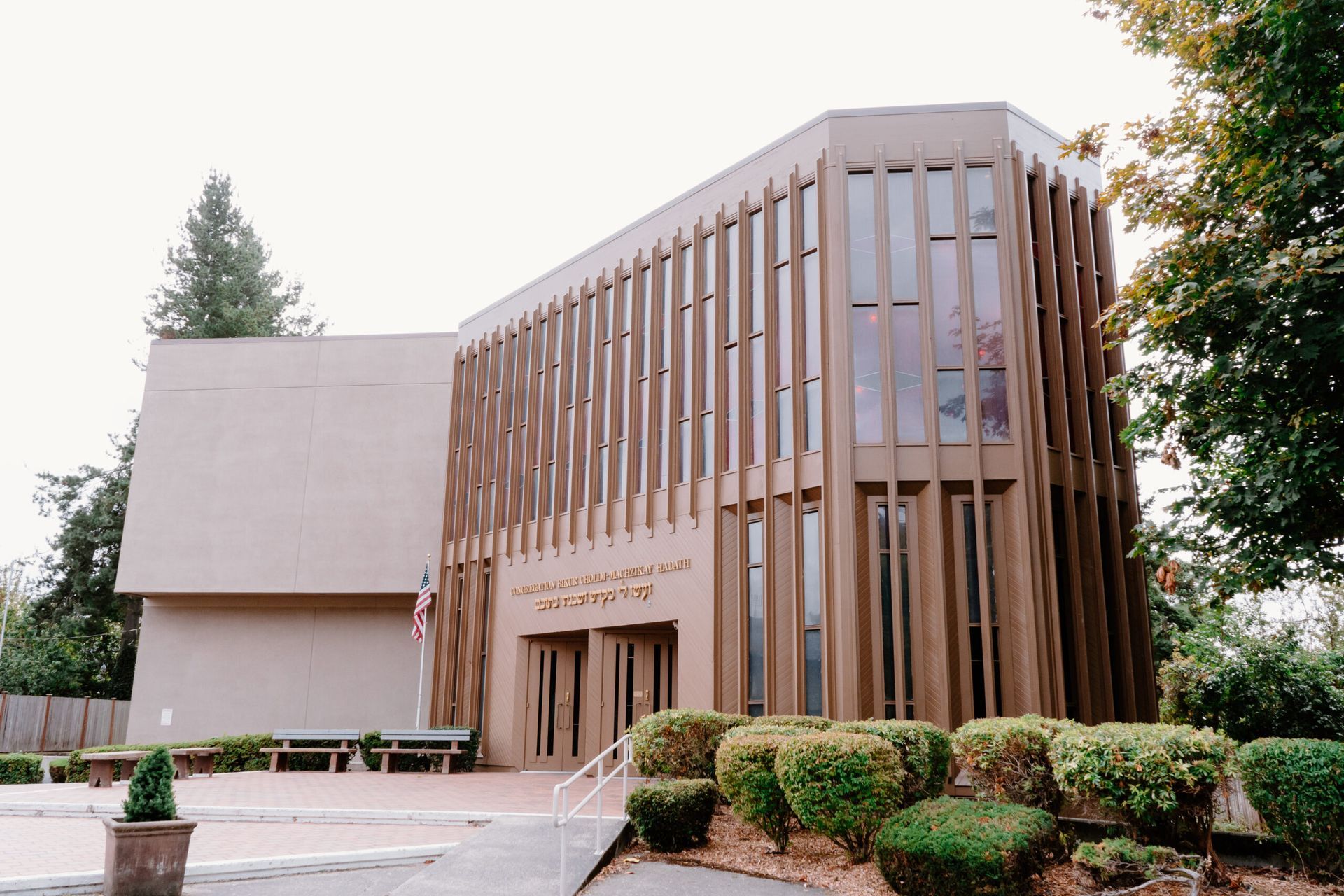 A large building with a lot of windows is surrounded by bushes and trees.