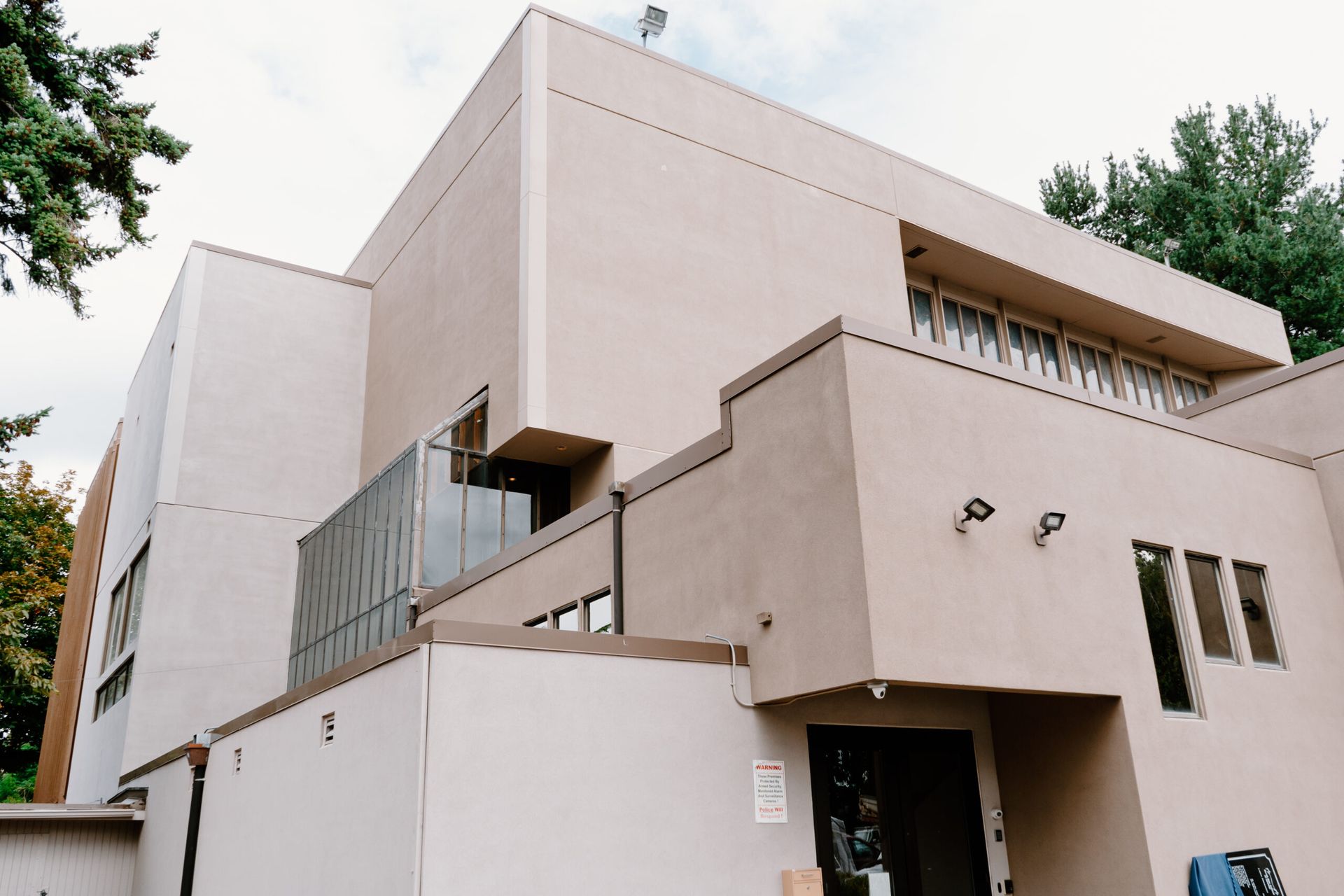 A large white building with a balcony and stairs is surrounded by trees.