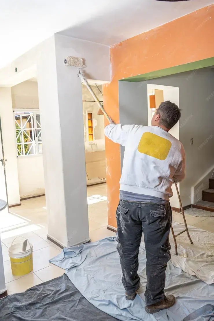 A man is painting a wall in a room with a paint roller.