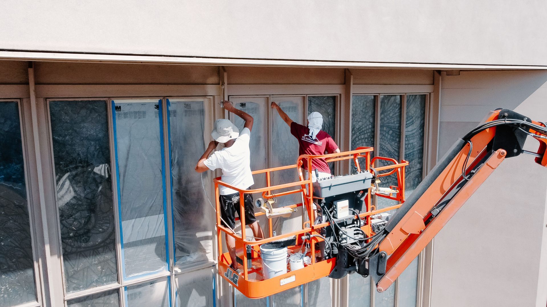 Two men are painting a building with a crane.