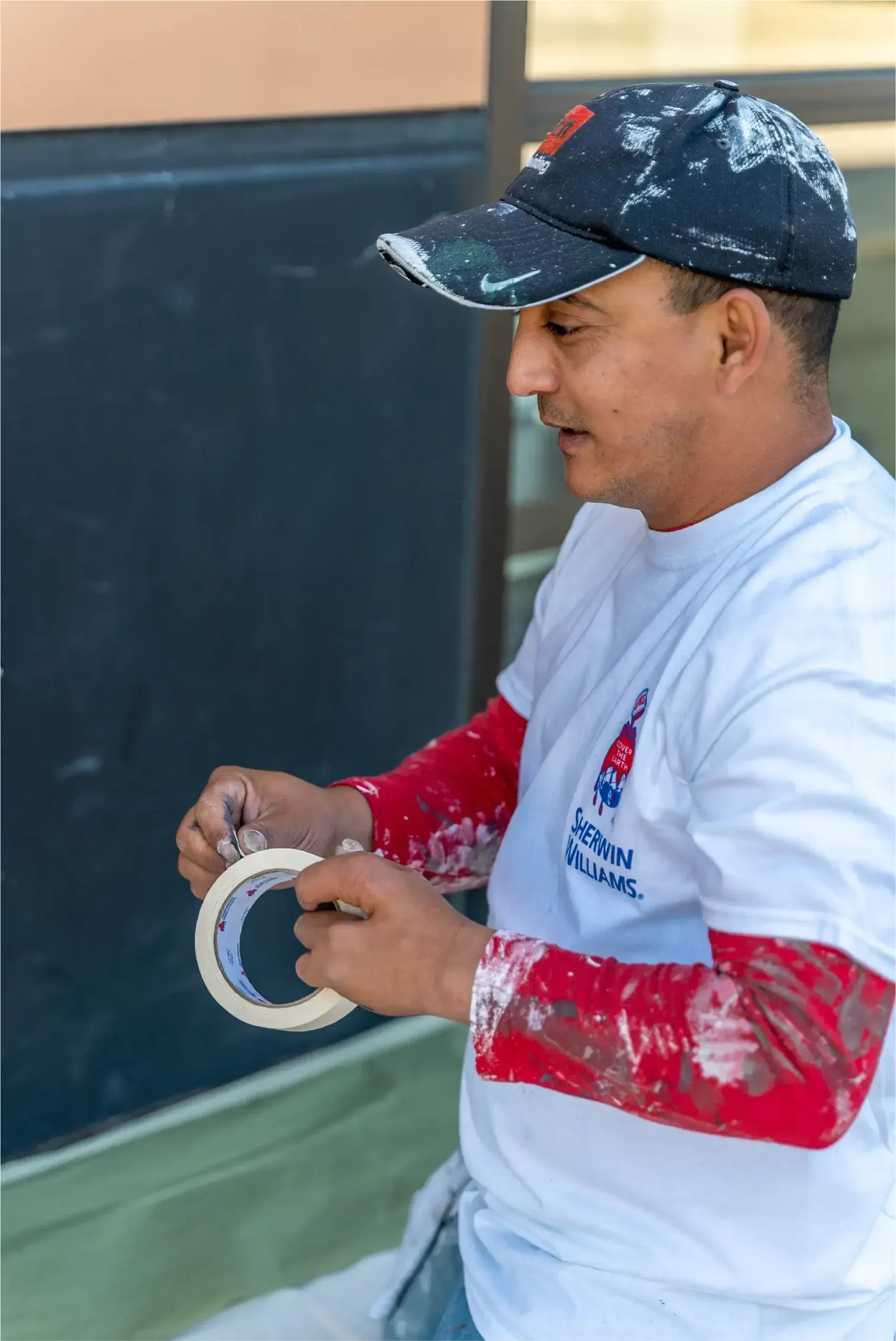 A man wearing a hat and a white shirt is holding a roll of tape.