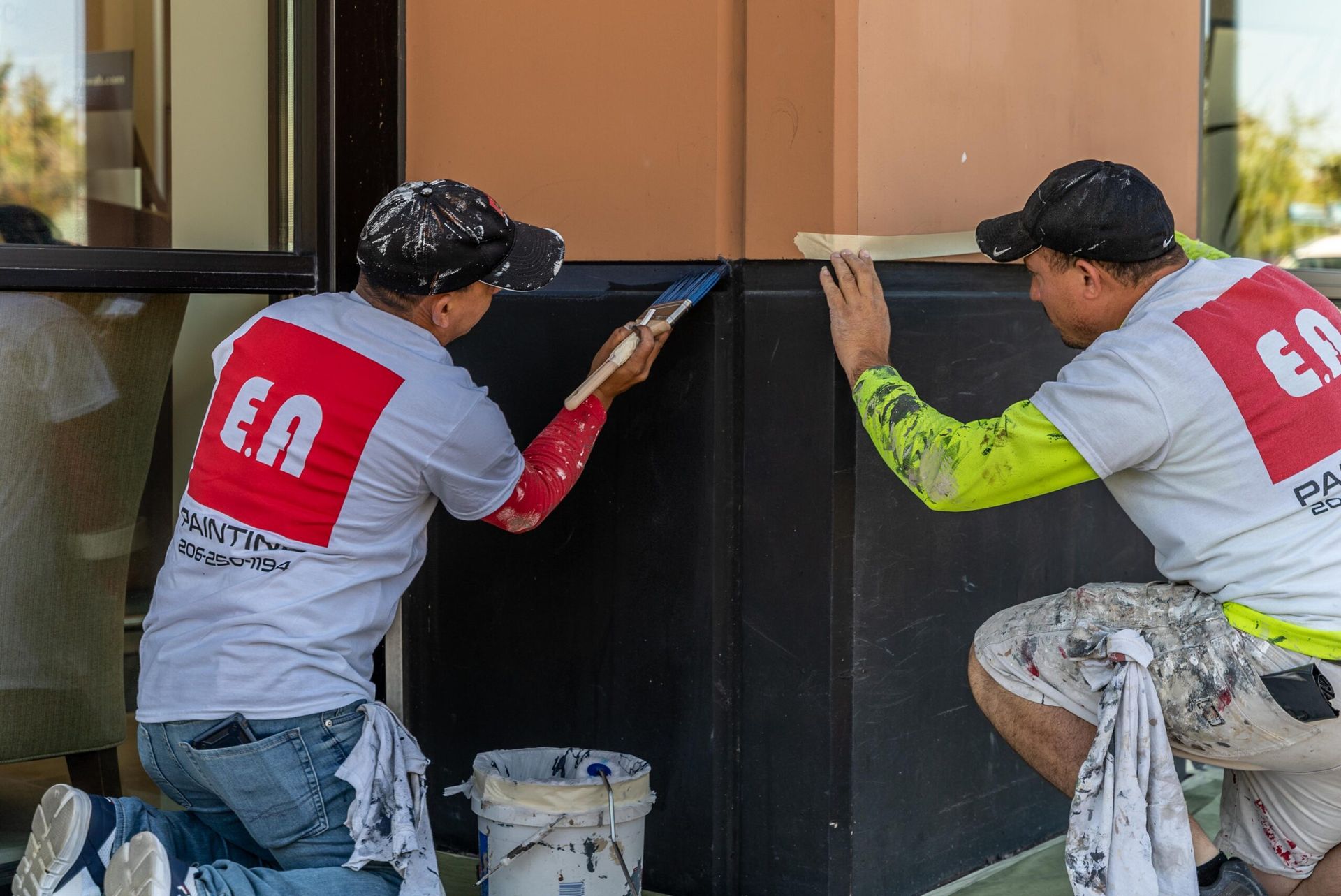 Two men are kneeling down and painting a building.