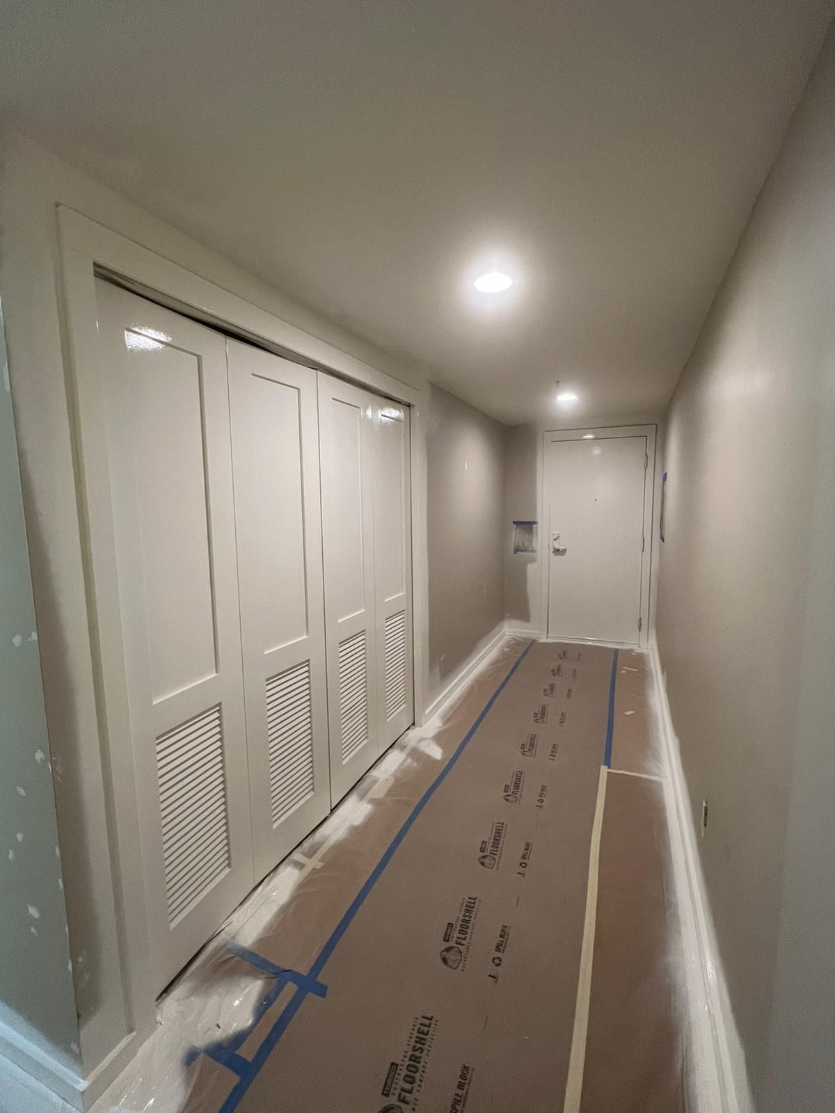 A long hallway with white doors and a blue tape on the floor.
