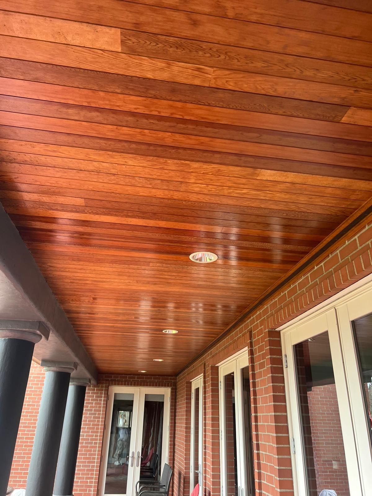 A porch with a wooden ceiling and a brick wall.