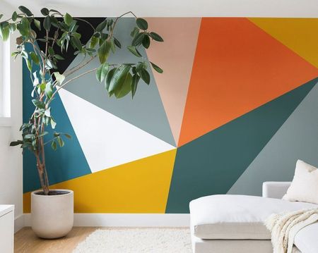 A living room with a couch and a plant in front of a colorful wall.