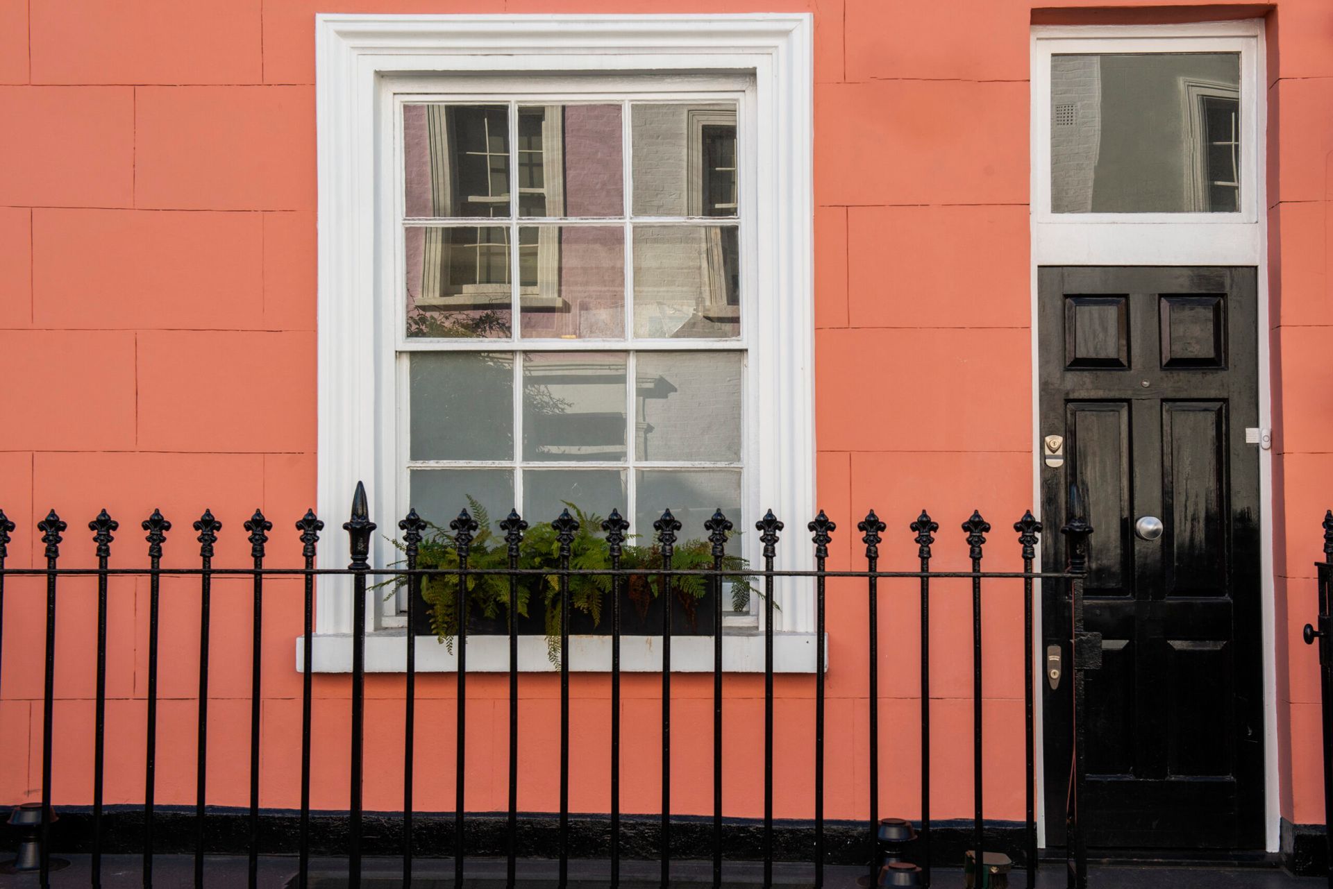 A pink house with a black fence and a black door.
