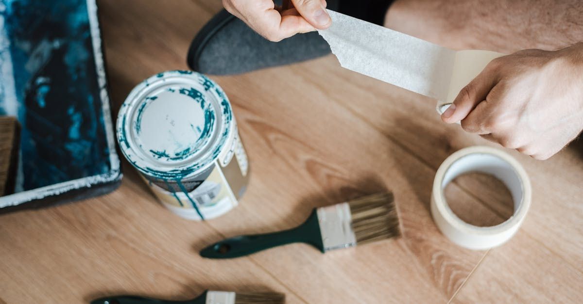 A person is taping a can of paint on a wooden floor.