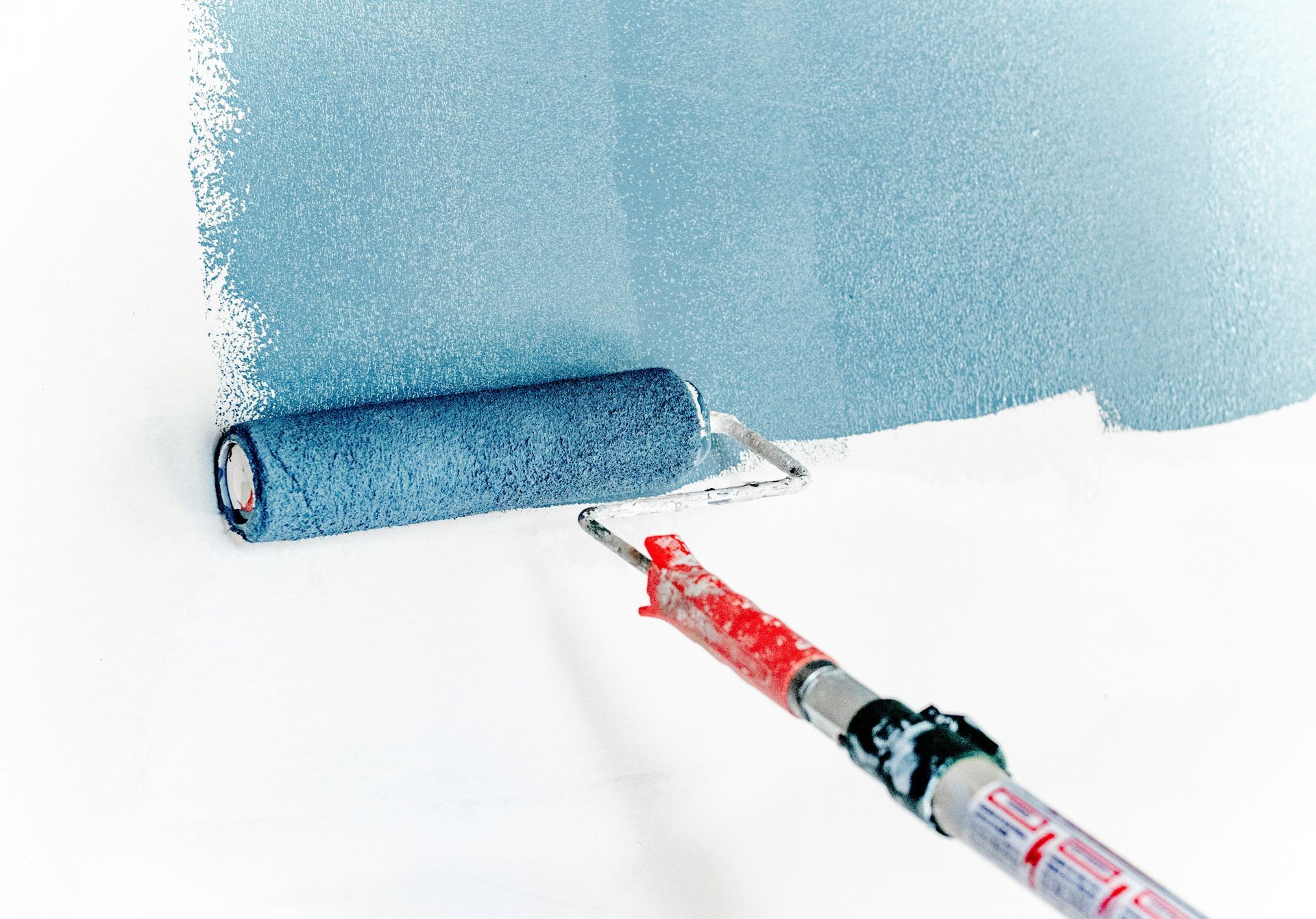 A blue paint roller is being used to paint a white wall.