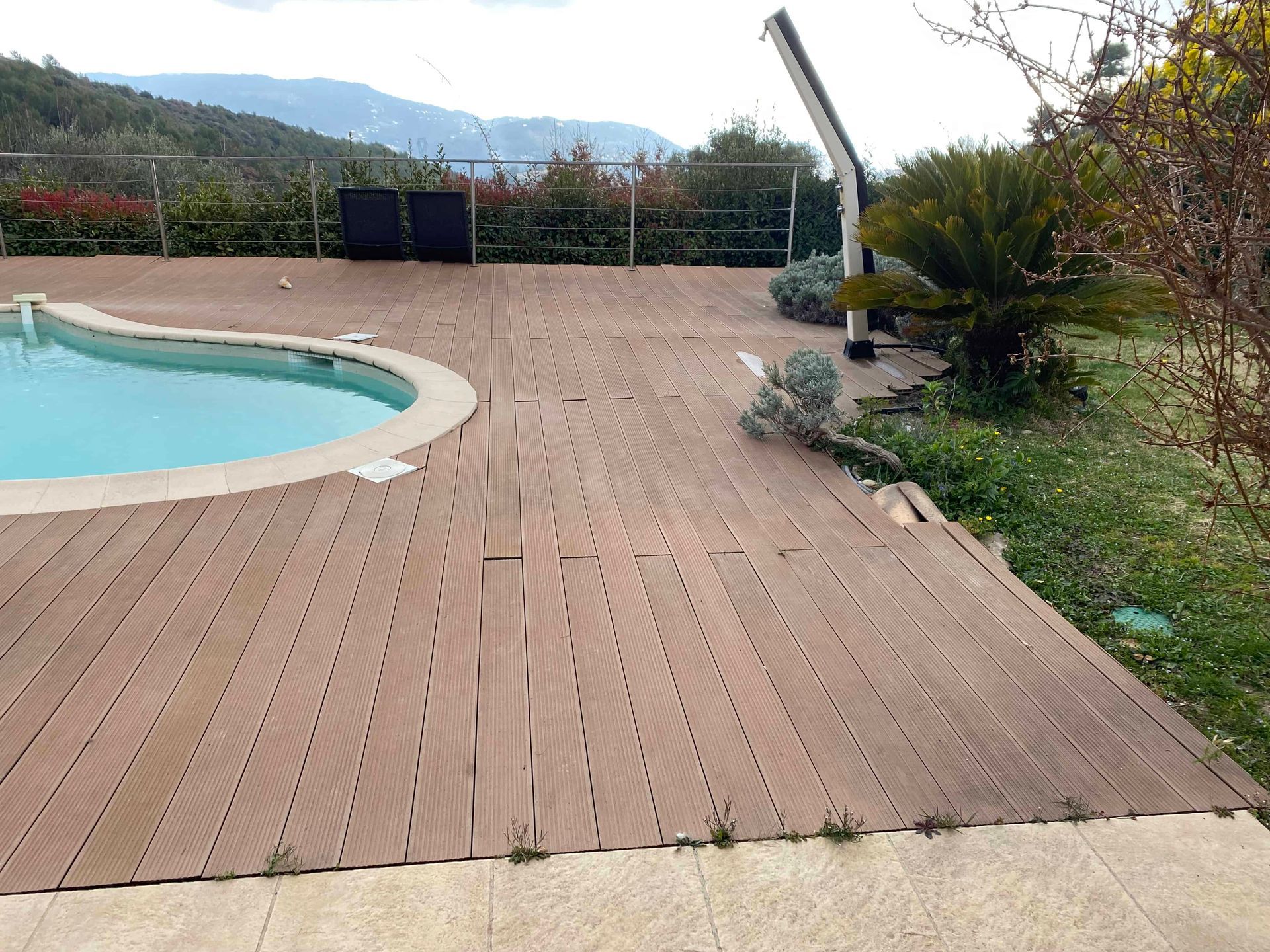 Une terrasse en bois avec une piscine en arrière-plan