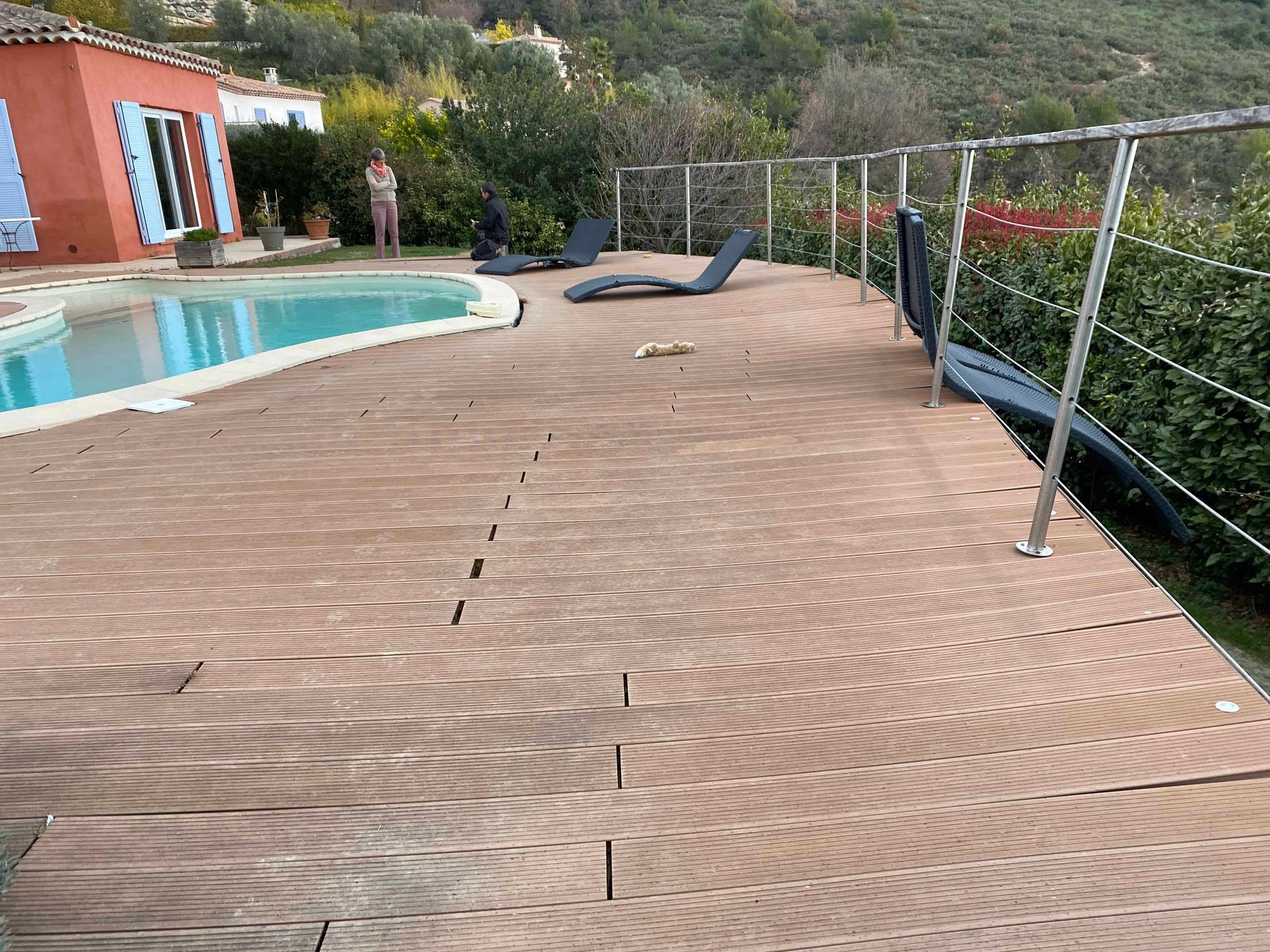 Une terrasse en bois avec une piscine en arrière-plan.